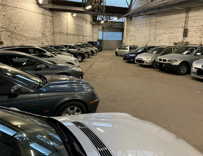 Parking Park Elite Valet - Samochody stoją w krytym pomieszczeniu. Ściany są z białej cegły. Oświetlenie jest sztuczne.