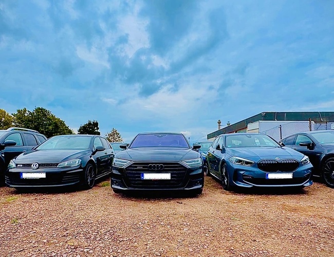 Prime Parking Valet – päť áut stojí na štrkovom nádvorí. Areál je obklopený ohradou. Na pozadí sú stromy a mraky.