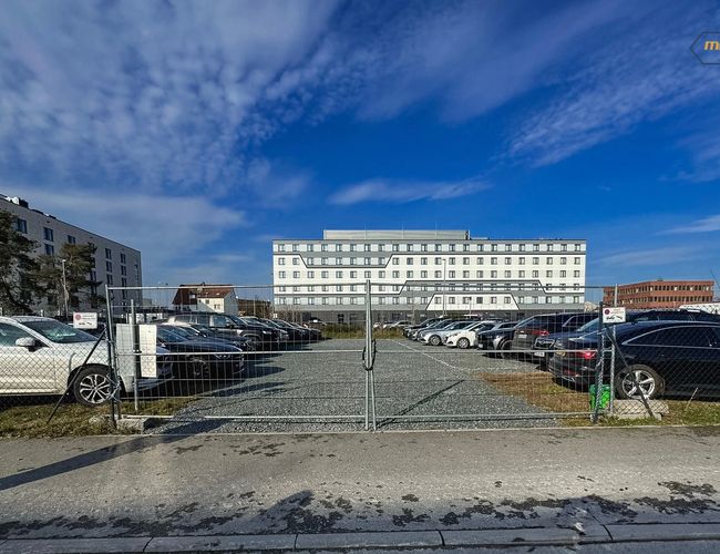 Parking Mein Valet Outdoor – teren ogrodzony, pełen zaparkowanych aut. W tle widać duży biały budynek.