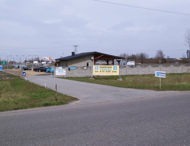 Estacionamiento VIAJE - Entrada al área pavimentada. Estacionamiento cercado con malla. A la entrada, edificio de recepción.
