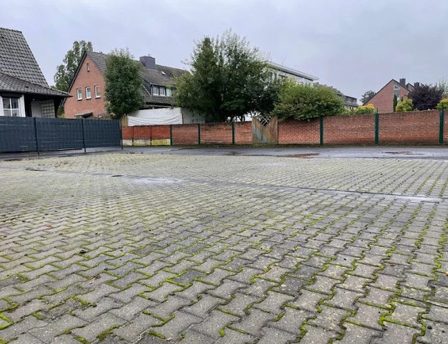 Parking My Travel Carpark Valet – Plac jest wyłożony kostką brukową. Otoczony jest ceglaną ścianą i metalowym ogrodzeniem. Drzewa rosną w tle.