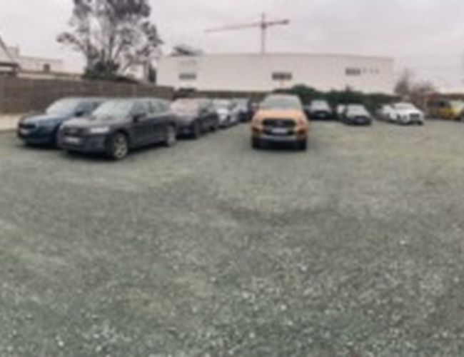 Parking Park-Box-Frankfurt Valet – Na parkingu stoją zaparkowane samochody. Teren jest otwarty i ogrodzony. W tle widać budynki i drzewa.