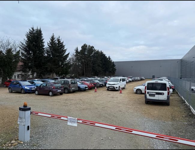 Feriebilparkering - Det står mange biler parkert her. Parkeringen er inngjerdet og ubearbeidet. Skyvedøren lukker adkomsten.