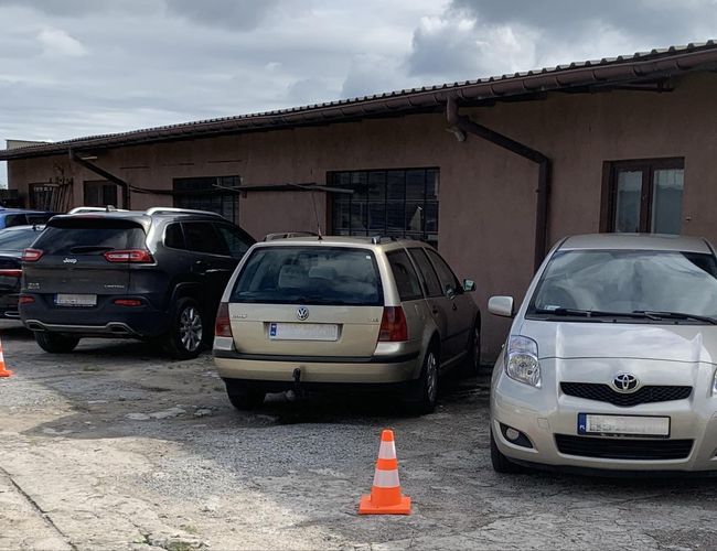 A1 Parking Max - Cztery samochody stoją przed budynkiem. Parking jest oznaczony pachołkami. Podłoże jest betonowe.