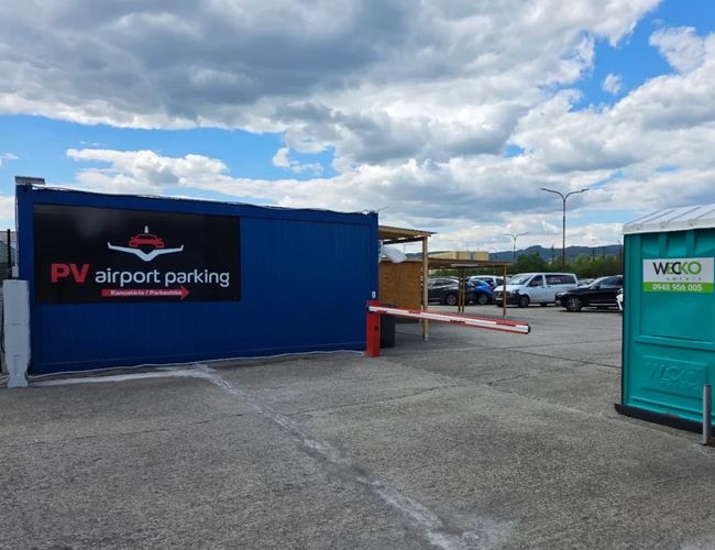 Wjazd na teren PV Airport Parking z widocznym oznaczeniem parkingu, punktem obsługi oraz miejscami parkingowymi dla samochodów klientów.