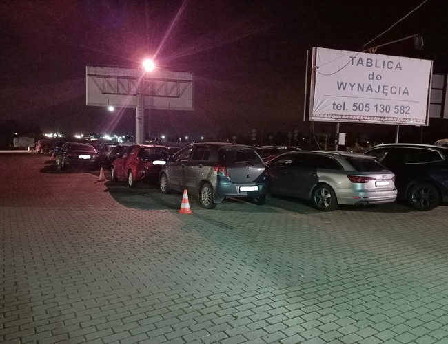 Parking MARTOM – En el patio hay muchos coches. El aparcamiento está iluminado por una lámpara. Se puede ver un letrero de alquiler de tablones.