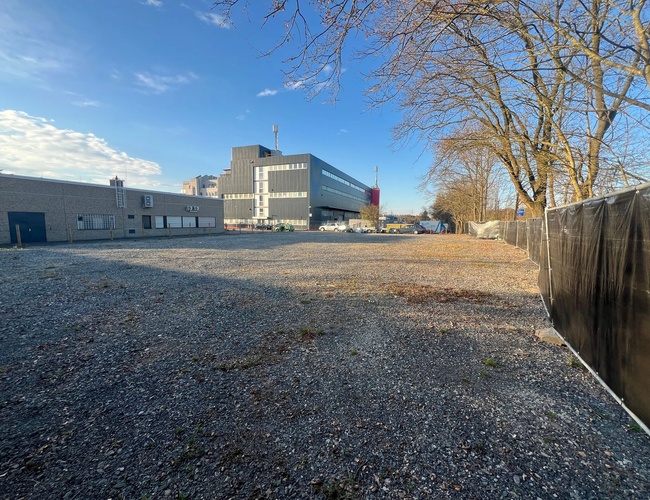 Parkovanie ParkPoint24 Valet - Veľké parkovisko so štrkovou povrchovou úpravou. Obklopené oplotením, v pozadí viditeľné budovy a stromy.