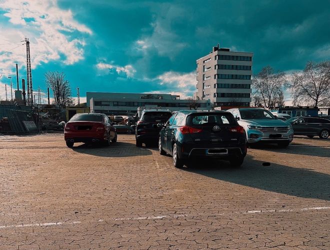 Parkolási biztonságparking24 VALET - Látható néhány parkoló autó. A háttérben egy magas épület áll. A parkoló kőburkolatú.