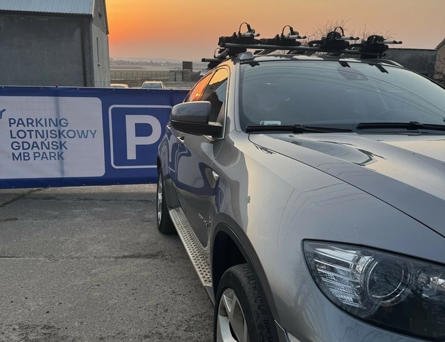 Parking MB Park – Szary samochód stoi na terenie parkingu. Widoczny jest zachód słońca nad budynkami.