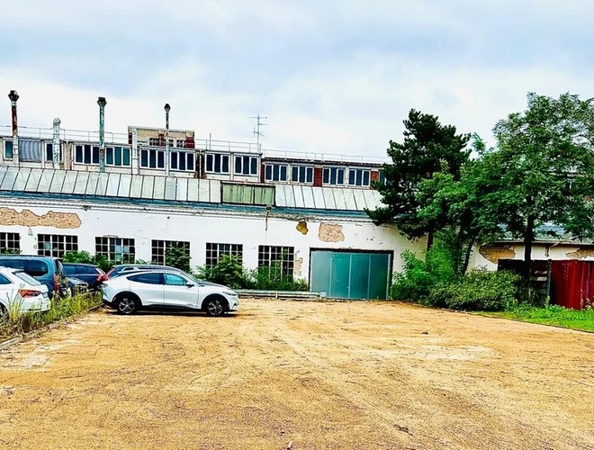 SchnellPark Valet - Kilka samochodów stoi na żwirowym placu. Teren jest ogrodzony. W tle widoczny jest budynek i drzewa.