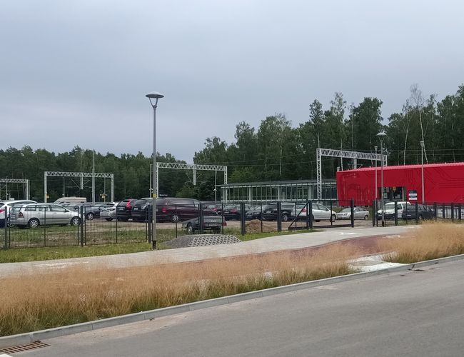 Smart parking – obszar z wieloma samochodami i czerwoną konstrukcją. Przestrzeń jest ogrodzona i ma widoczne oświetlenie. W tle drzewa.