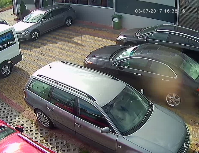 PARKING P24 PREMIUM – Kilka aut stoi na wyłożonym kostką placu. Teren jest ogrodzony i przy budynku.