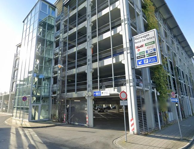 Widok na budynek parkingu Parkenplus z przeszkloną fasadą, oznakowaniem oraz wjazdem do wielopoziomowego parkingu.