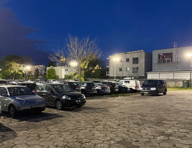 Widok samochodów zaparkowanych na parkingu nocą. Dobrze oświetlony plac.