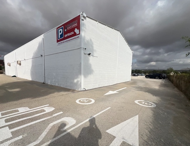 Parkeringsplass Punta Marina - Stor hvit bygning ved parkeringsplassen. På bakken er merkinger og piler synlige. I bakgrunnen er det flere parkerte biler.