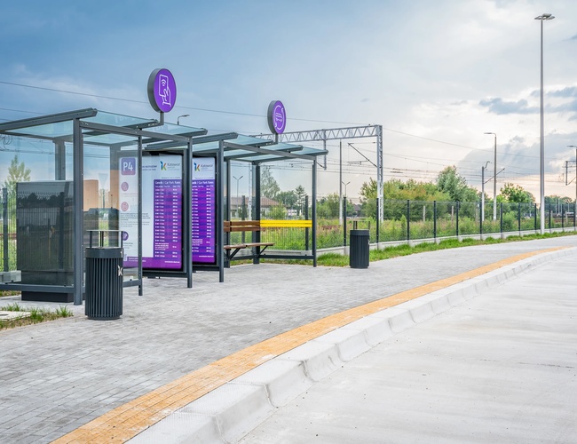 Aparcamiento Oficial P4 - Modernas paradas de autobús con información. El área está cercada. En el fondo se ven las vías del tren.