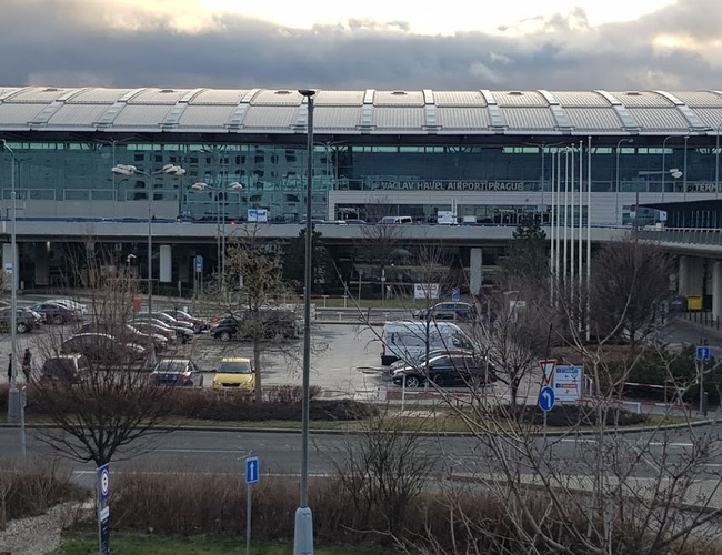 Parkovisko Smile Parking – je viditeľné veľké, otvorené parkovisko. V pozadí sa nachádza moderná budova terminálu letiska. Atmosféra je zamračená.