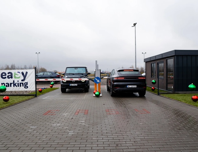 Jednoduché parkovanie štandard - dve autá stoja pri závoru. Na pravej strane je tmavá budova. Na trávnikoch sú farebné gule.