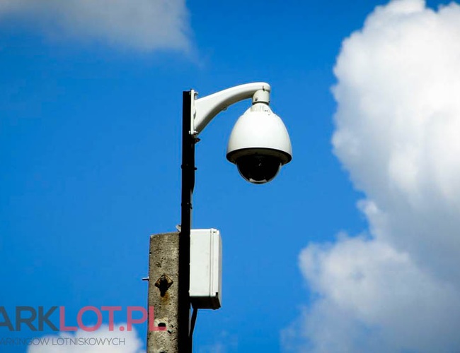 Parkovisko P38 - Na stĺpe je namontovaná monitorovacia kamera. Pozadie tvorí obloha s bielymi oblakmi.