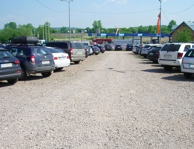 Orange Parking P3 - Teren żwirowy z zaparkowanymi autami po dwóch stronach. Parking nie jest ogrodzony. W tle widać zieleń i budynki.