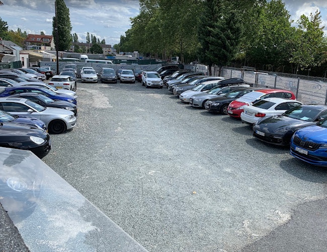 Parkovisko Parkparadies – Na námestí stojí veľa áut v dvoch radoch. Areál je otvorený a obklopený stromami a plotom.