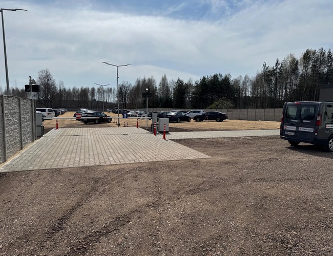 SkyParking - El parking está cercado y iluminado. Al fondo hay coches. El terreno está pavimentado y es espacioso.