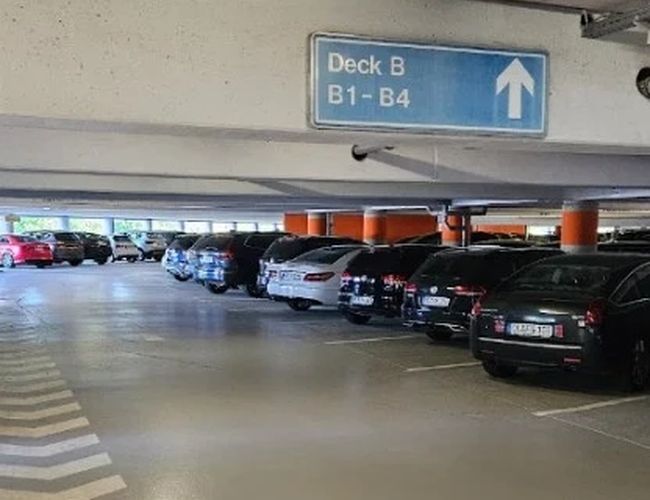 Wnętrze parkingu wielopoziomowego z szerokimi alejkami, oznakowaniem poziomów oraz rzędami zaparkowanych samochodów ułatwiającymi orientację.