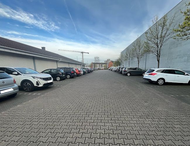 Parkering Mein-Flughafenparkplatz-Frankfurt P2 - Biler står på begge sider av asfaltert vei. På høyre side ser du trær, og på venstre side en bygning.