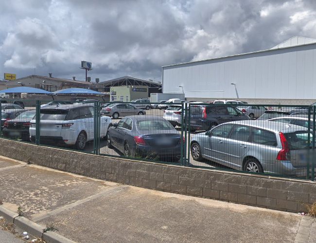 Estacionamiento Park and Greet Valet - en la imagen se puede ver un estacionamiento cercado con coches estacionados. Al fondo hay edificios industriales.