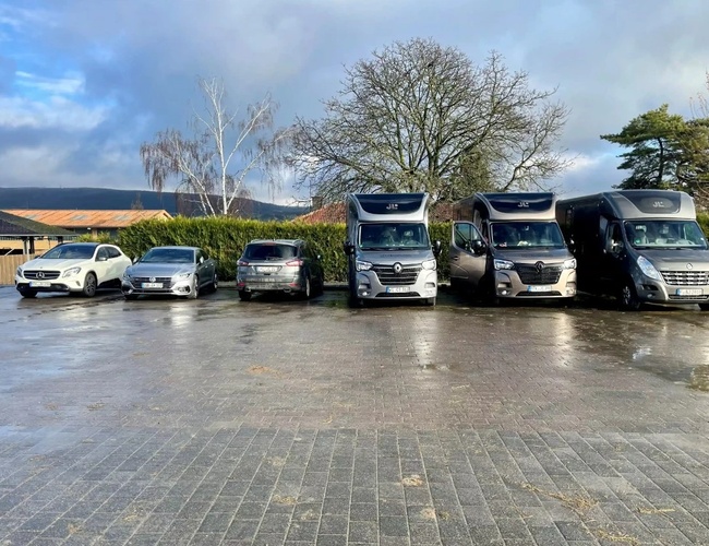 Parkovisko ParkNow Frankfurt – Šesť zaparkovaných vozidiel na voľnom priestranstve. Na pozadí sú stromy a kríky. Areál je upravený z kameňov.