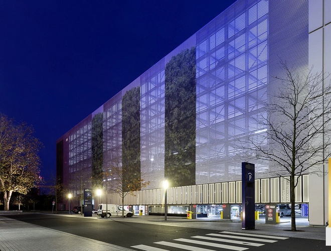 Parken Mein-Flughafenparkplatz-Frankfurt ShortWay – modernes Parkhaus. Die Fassade ist metallisch und grau. Es sind Schilder und Bäume sichtbar.