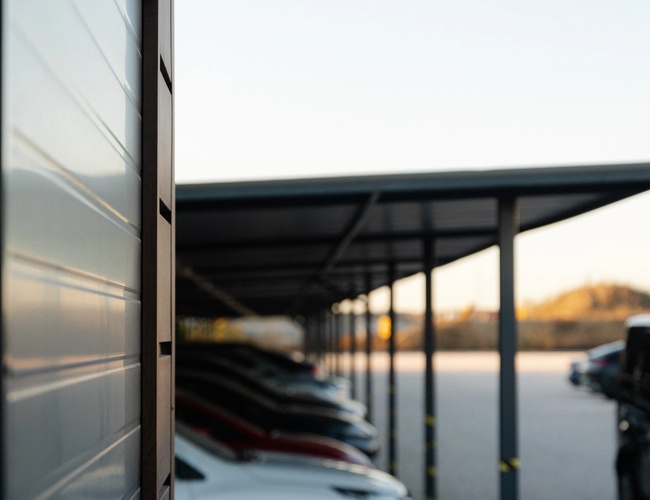 Widok wzdłuż zadaszonych miejsc parkingowych z zaparkowanymi samochodami osobowymi