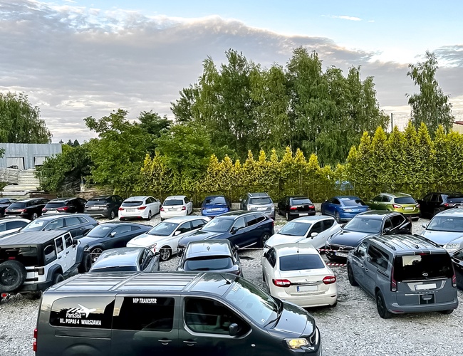 Parksist – parkovisko plné áut. Pozemok obklopený stromami. Povrch štrkový.