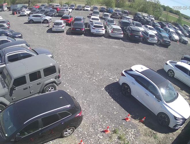 TRIP Parking – Oplotené miesto s búdkou a autom. Na sieti je veľký informačný banér. V pozadí je vidieť niekoľko zaparkovaných áut.