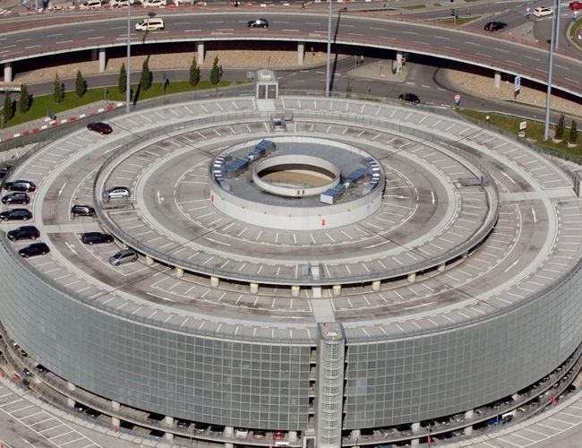Widok z lotu ptaka na okrągły wielopoziomowy parking P2 z centralną rampą oraz drogami dojazdowymi otaczającymi obiekt.