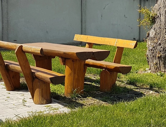 Drewniany stolik z ławkami ustawiony na trawniku przy drzewie, w słoneczny dzień.