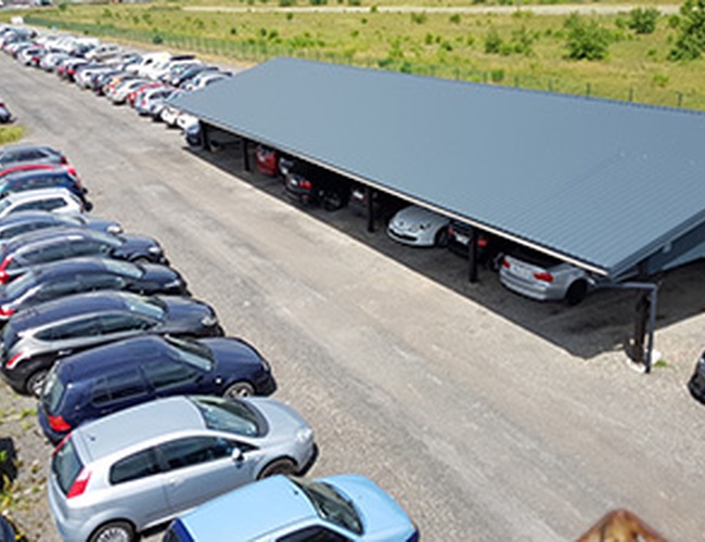 Parkovisko MTM - Na parkovisku stojí veľa áut. Je tam zastrešená precedent. Vedľa je trávnaté prostredie.