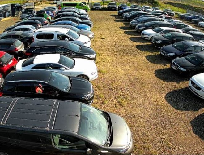 Grand Parking - Teren jest zapełniony samochodami. Parking ma żwirową nawierzchnię. Samochody stoją w równych rzędach.