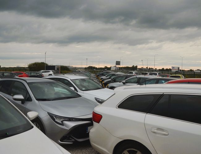 Royal Parking – Na zdjęciu widoczne są zaparkowane samochody. Niebo jest pochmurne. Teren jest ogrodzony i przestronny.