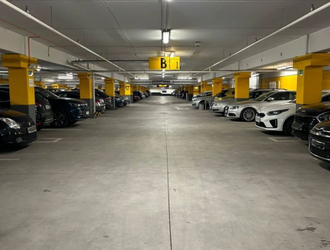 Parking MarcelinPark - Podziemny parking z wieloma autami po obu stronach. Sufit ma świetlówki, a kolumny są żółte.