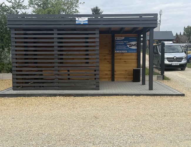 FlyParking - Przed wejściem stoi zadaszona poczekalnia. W tle widać zaparkowany samochód. Plac jest pokryty żwirem.