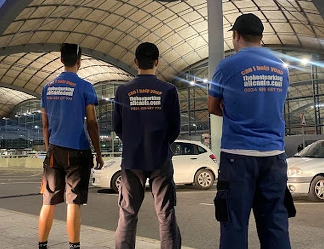 Najlepší vonkajší parkovací servis Alicante - Traja zamestnanci stoja čelom k modernému objektu. Majú na sebe modré košele s logom firmy. V pozadí je vidieť parkovisko.