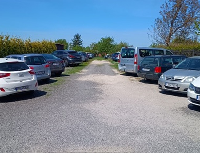 Parking Park24 - Camino de grava entre coches estacionados. Los vehículos están en dos filas. Al fondo se ven árboles y arbustos.