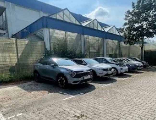 Samochody zaparkowane na brukowanym placu obok budynku z niebieskimi konstrukcjami dachowymi.