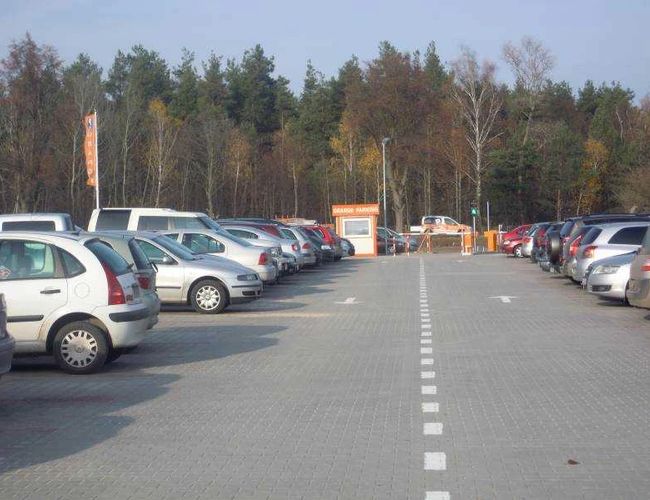 Orange Parking Modlin - En el aparcamiento hay filas de coches. El terreno está pavimentado con adoquines. Al fondo se pueden ver árboles y un puesto de aparcamiento.