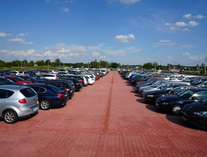MEGA Parking - Parking z kostki brukowej. Samochody ustawione w rzędach. W tle zieleń i niebo.