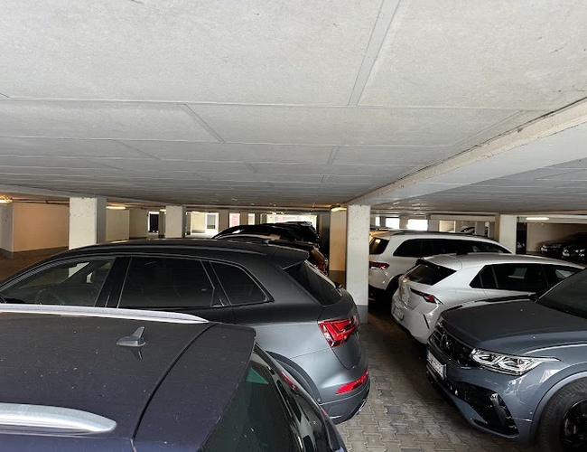 Parking Marspark Covered Valet – zadaszony parking pełen samochodów. Jasne światło oświetla wnętrze pomieszczenia.