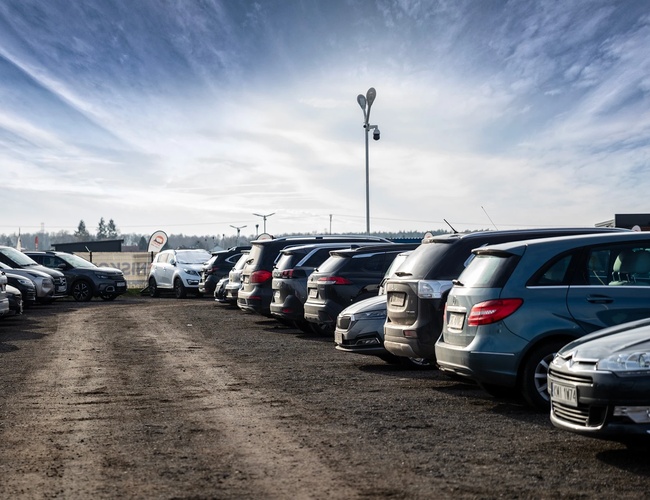 Parkovisko Okęcie Južné - Automobily stoja na spevnenej ploche. Na pozadí sú viditeľné lampy a informačná tabuľa.
