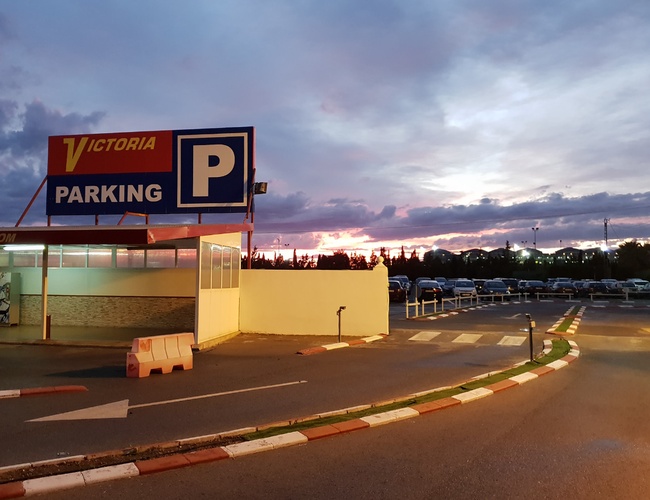 Victoria Parking Walencja - Duży parking zadaszony i oznakowany. W tle widać wiele zaparkowanych aut. Na niebie jasne kolory zachodu słońca.