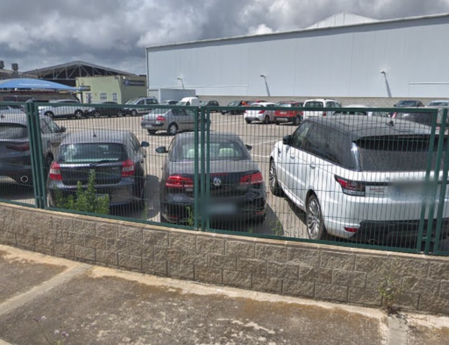 Parking Park and Greet Valet – el área está cercada. Se pueden ver coches de diferentes marcas aparcados. Junto al aparcamiento hay un gran edificio.